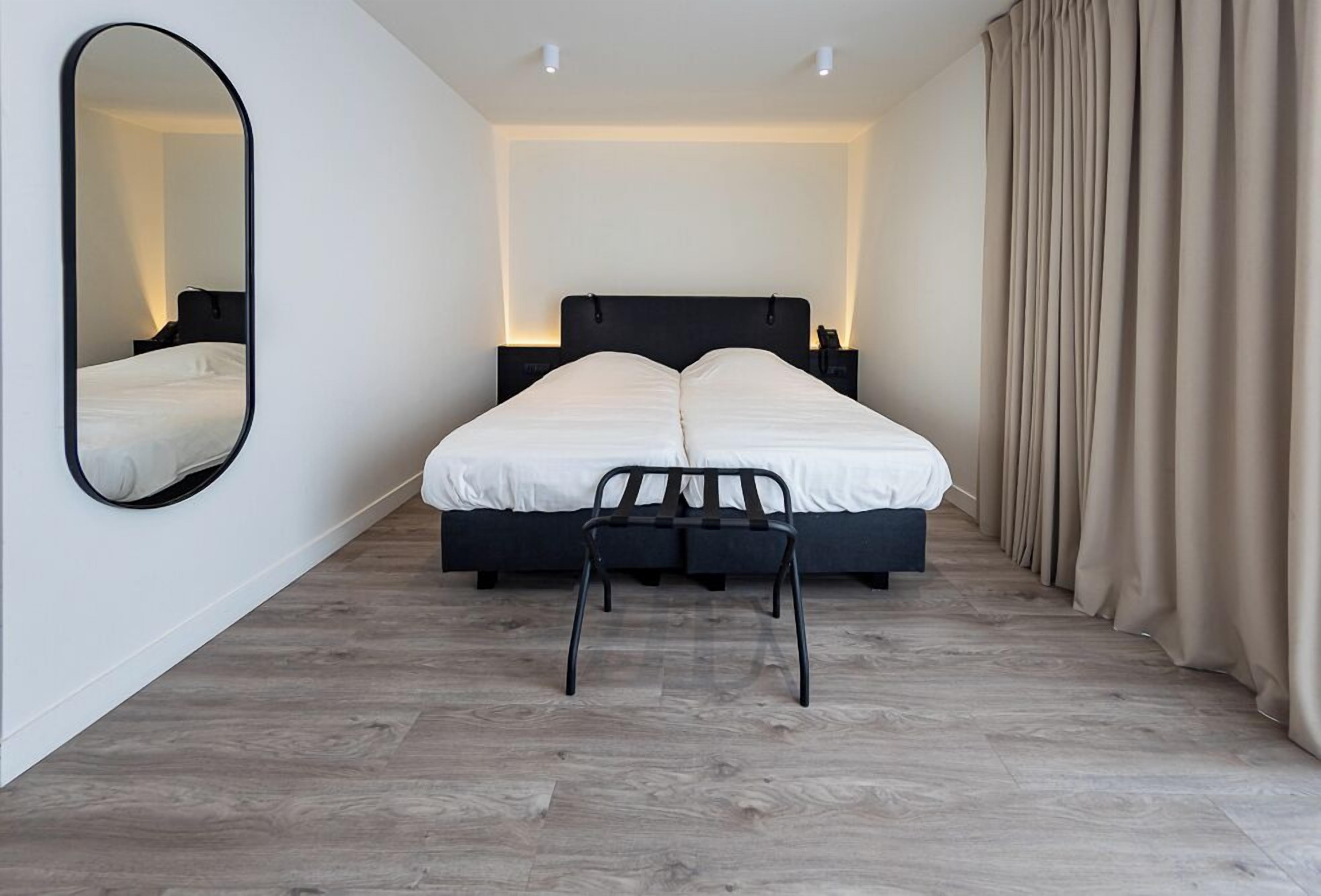 A modern bedroom with a bed, a chair, a mirror, and a nightstand.