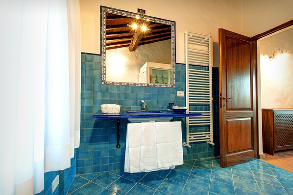 Un baño con piso de azulejos azules, un lavamanos con encimera azul, una toalla blanca colgada en un perchero y una puerta de madera.