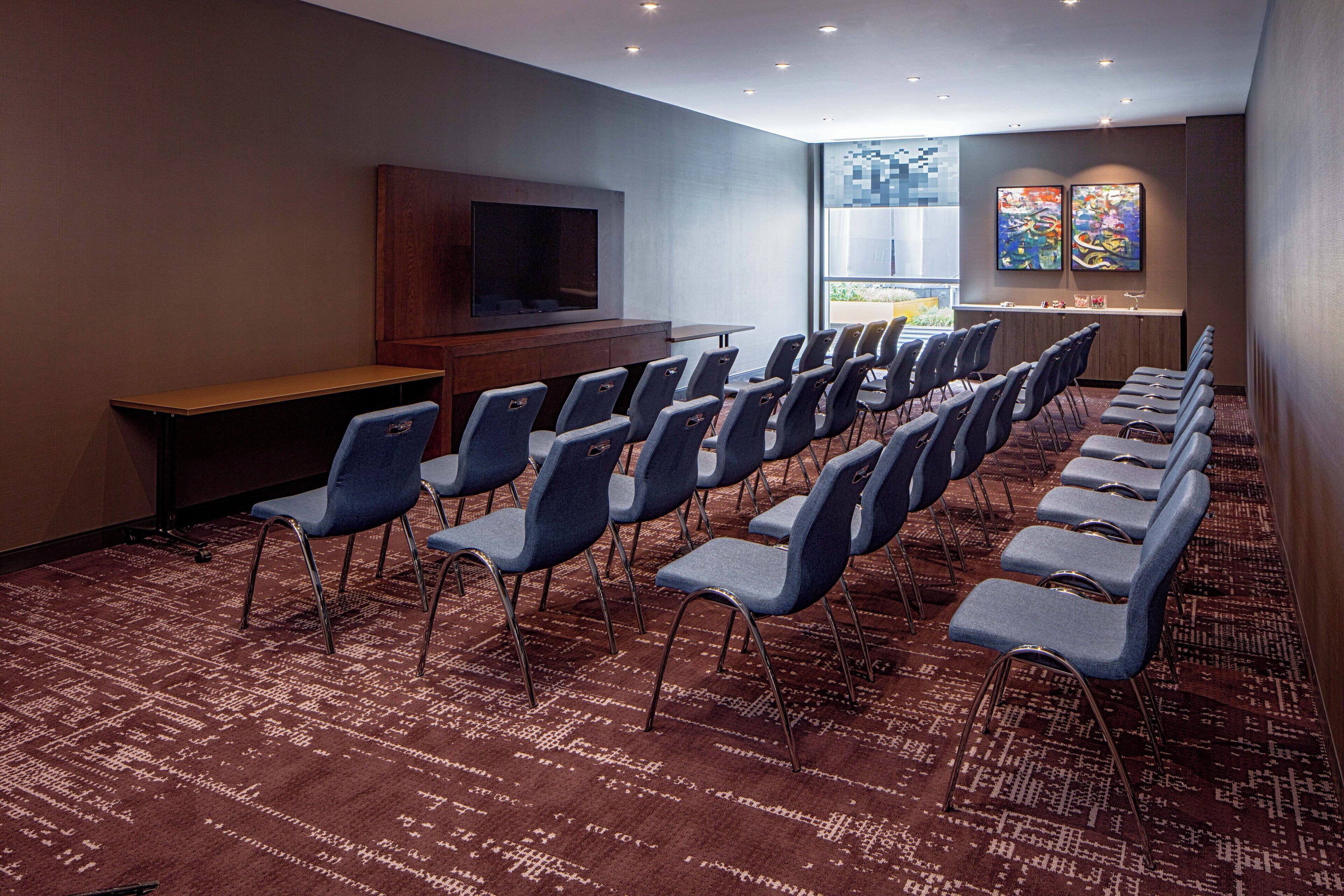 A conference room with rows of chairs, a large flat-screen TV, and a carpeted floor.