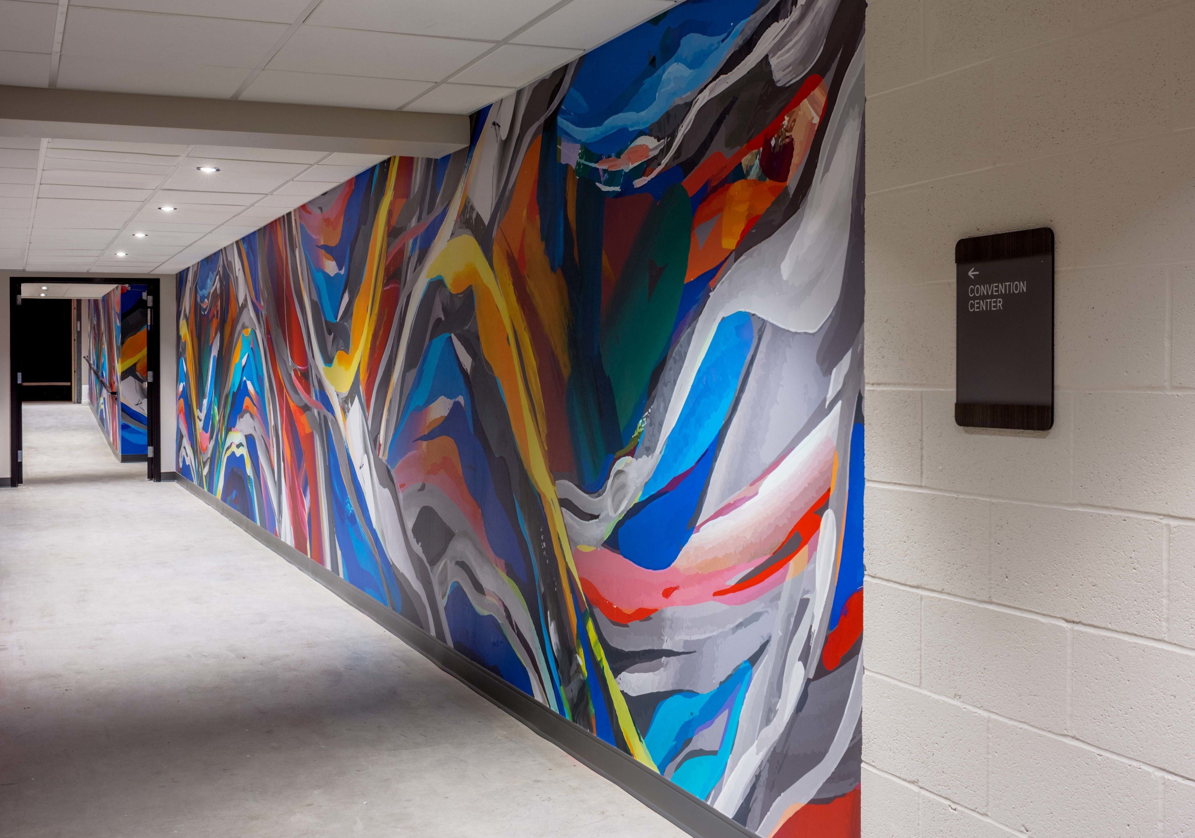 Un passadís amb un mural abstracte i colorit a la paret i un senyal que indica el camí cap al centre de convencions.