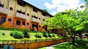 Un edificio de varios pisos con balcones, un sendero pavimentado y abundante vegetación.
