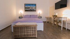 Un dormitorio con cama, mesitas de noche, escritorio, silla, televisor y un cuadro en la pared.