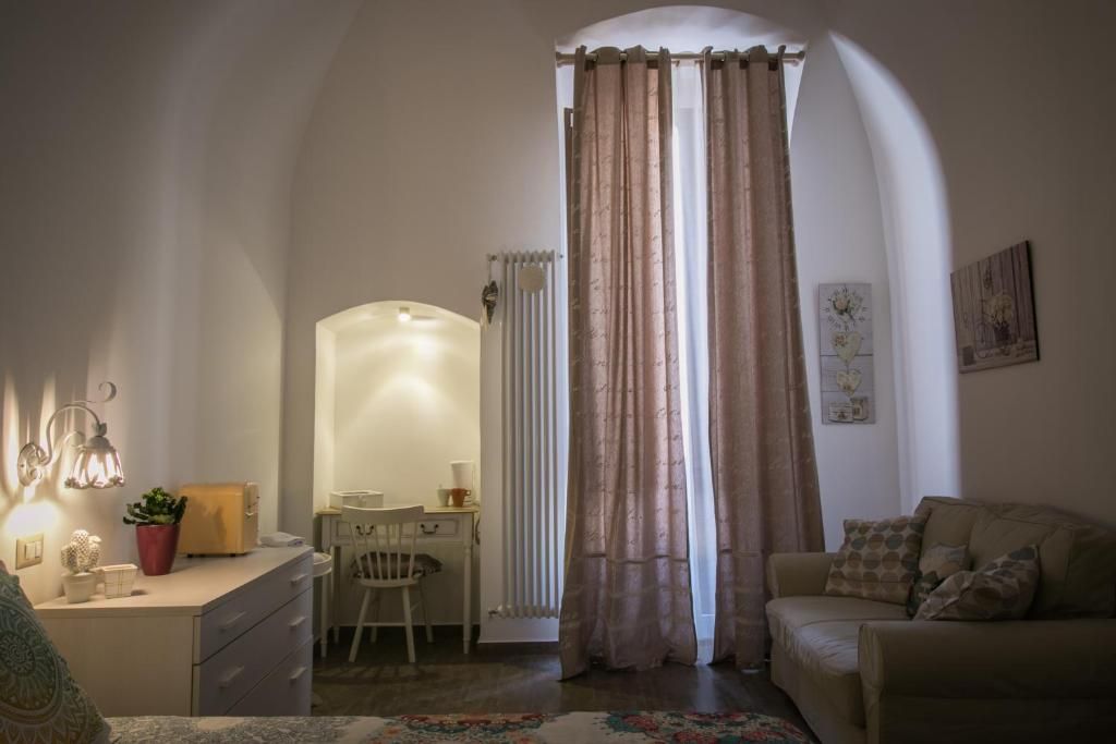 A cozy living room with a sofa, a desk with a chair, a radiator, and a window with curtains.