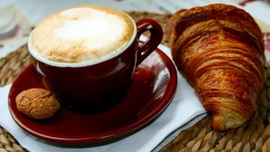 Una taza roja de café con espuma, un croissant y una galleta sobre un posavasos tejido.