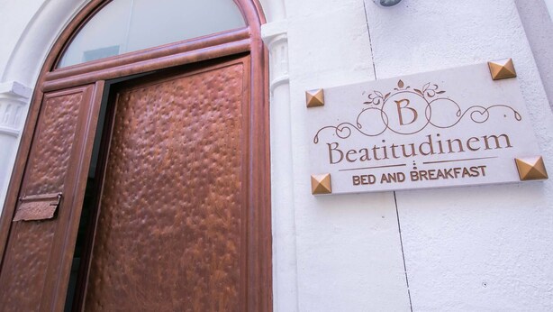 Letrero de 'Beatitudinem Bed and Breakfast' con una puerta marrón y una pared blanca.