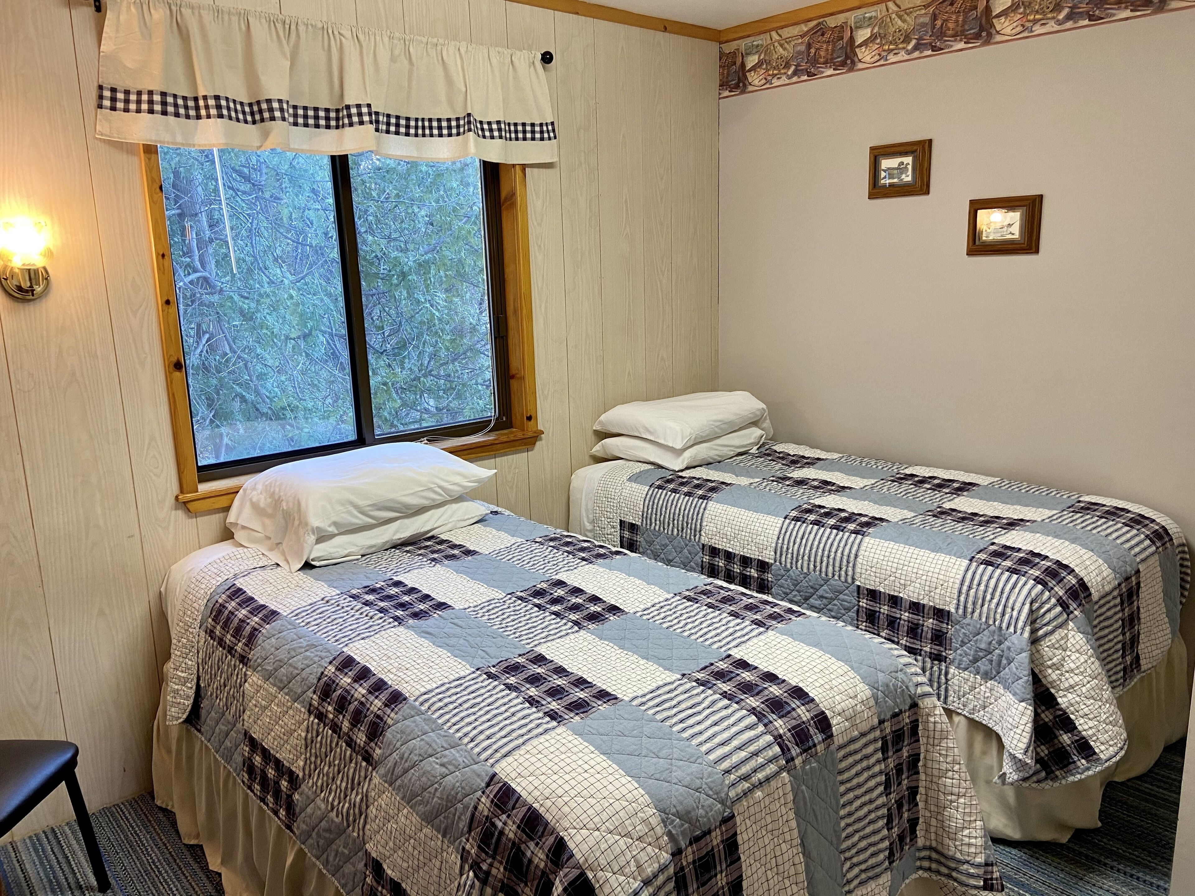 Une chambre avec deux lits, une fenêtre donnant sur les arbres et un mur orné de tableaux.