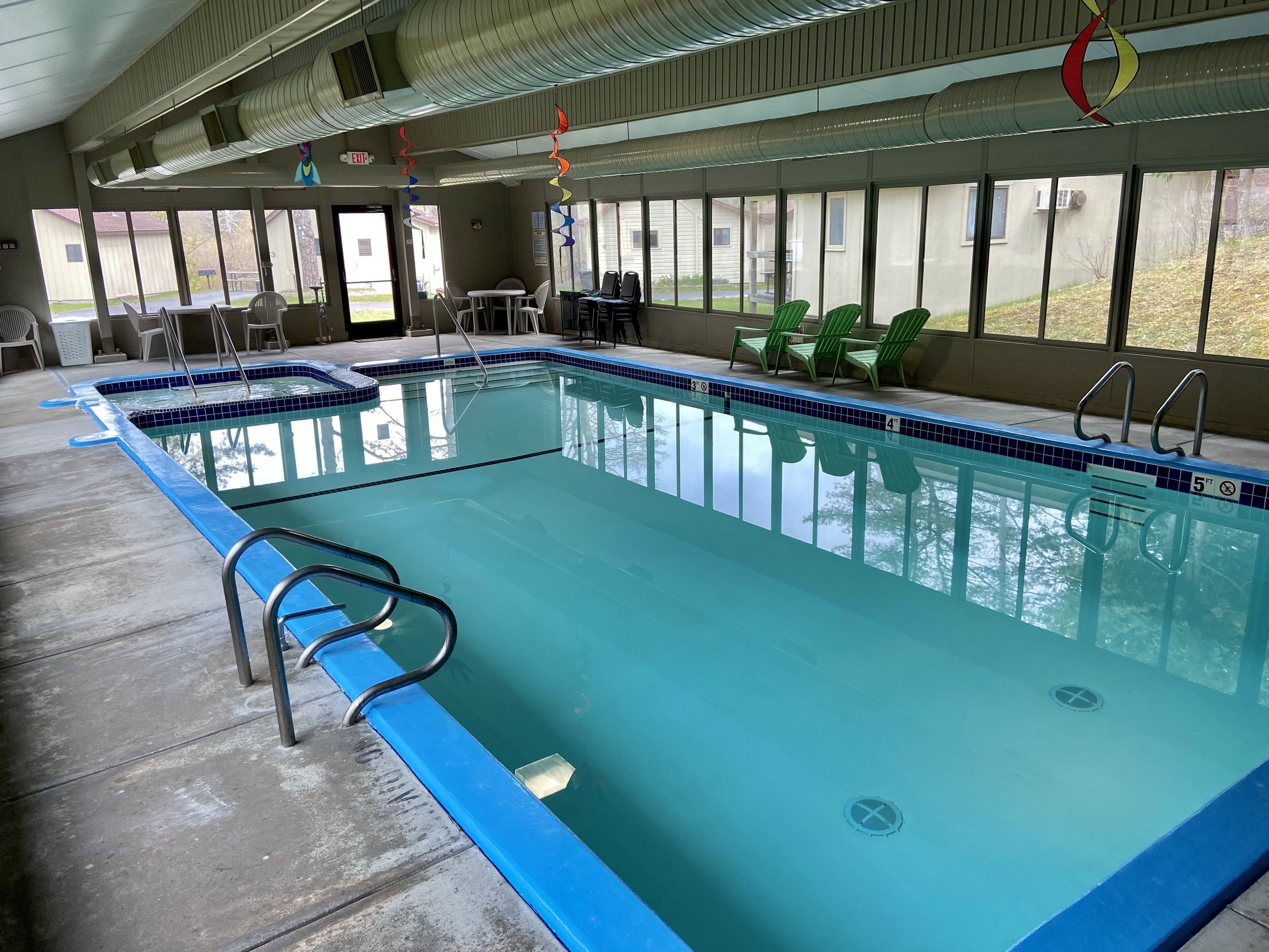 En stor indendørs swimmingpool med klart vand, omgivet af liggestole og borde.