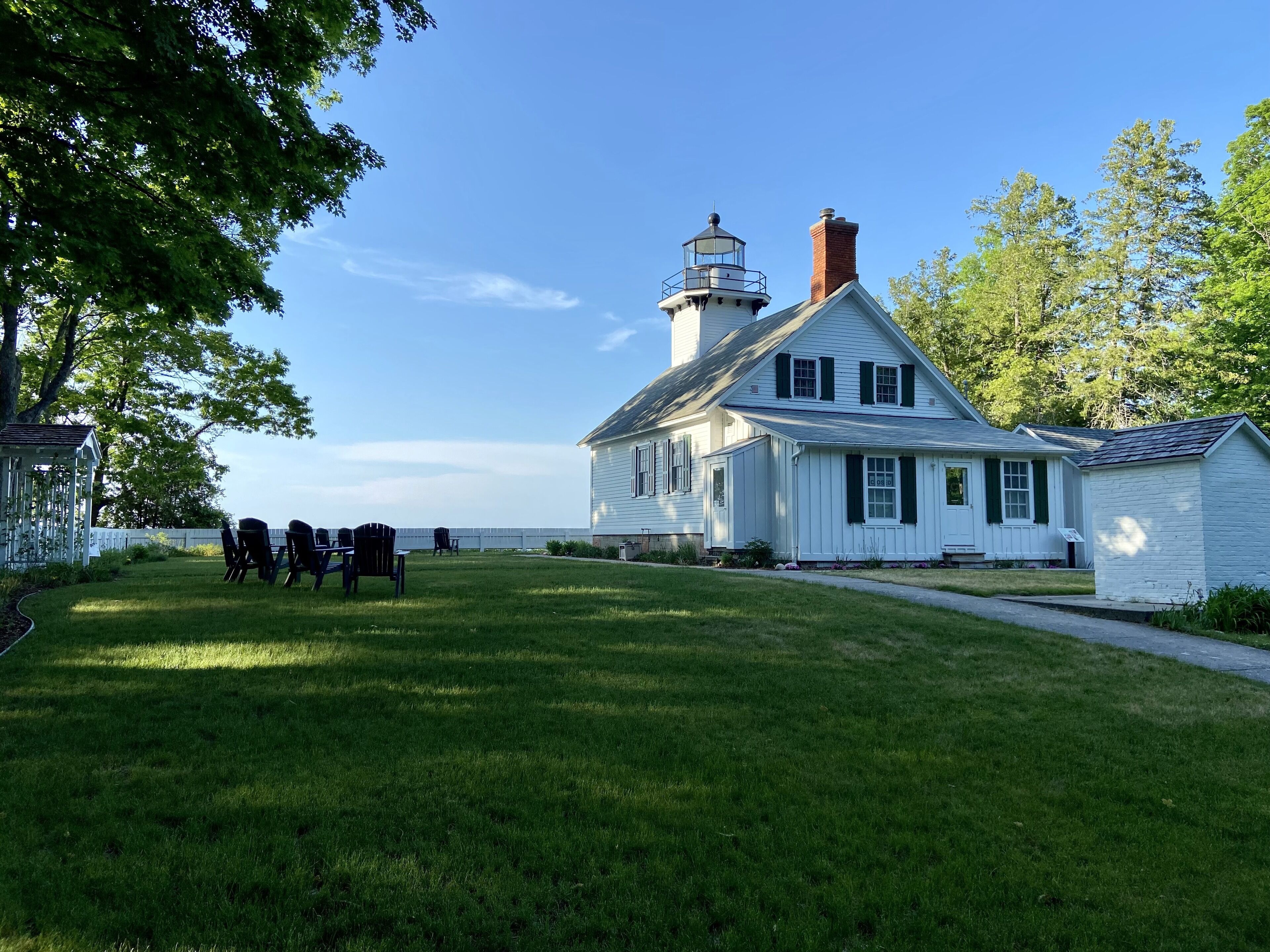 Un bâtiment blanc surmonté d’une tour de phare, avec une pelouse verdoyante et une vue sur l’eau.