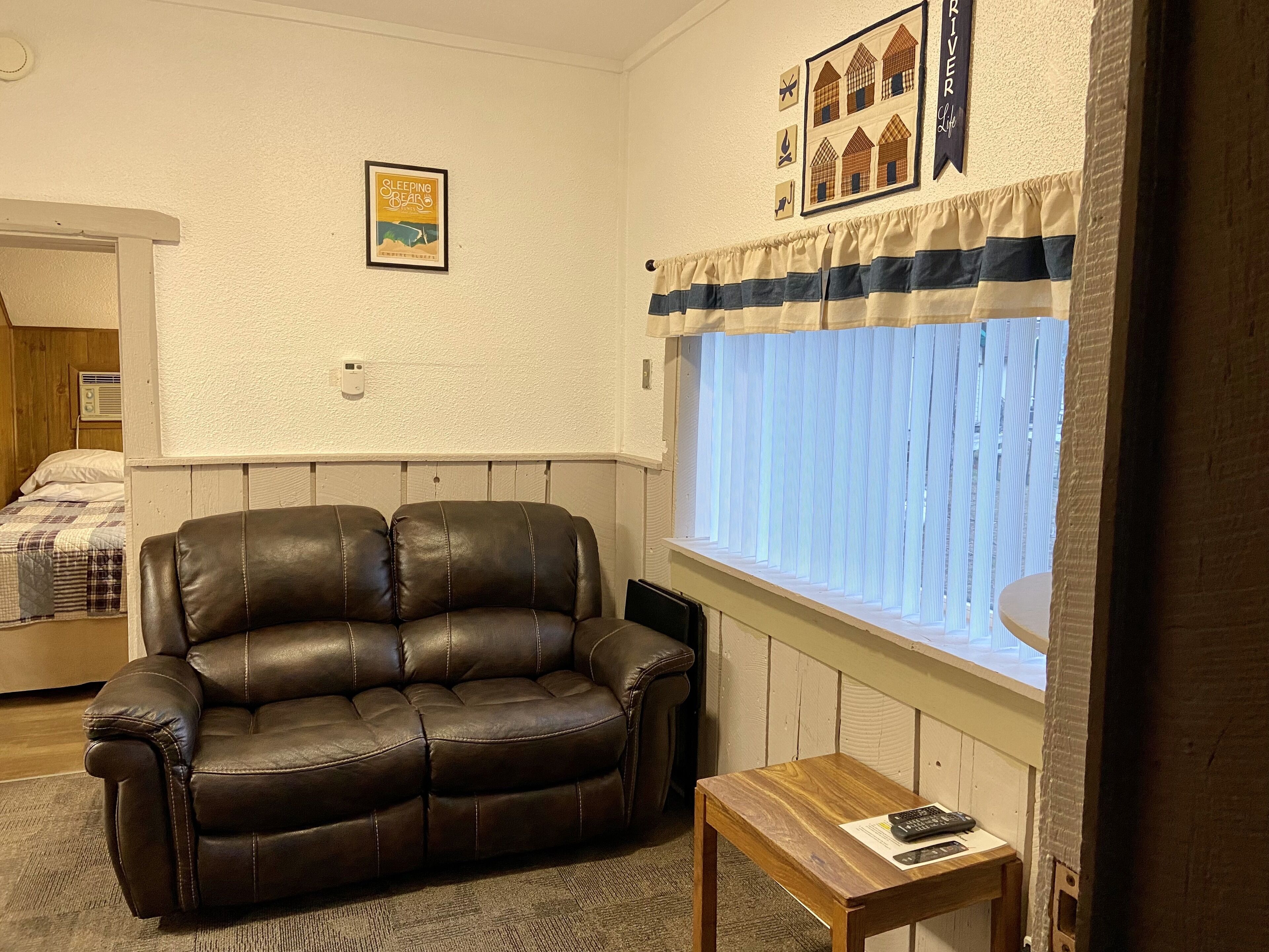 Un salon avec un canapé en cuir marron, une petite table en bois, une fenêtre avec des rideaux et un radiateur fixé au mur.