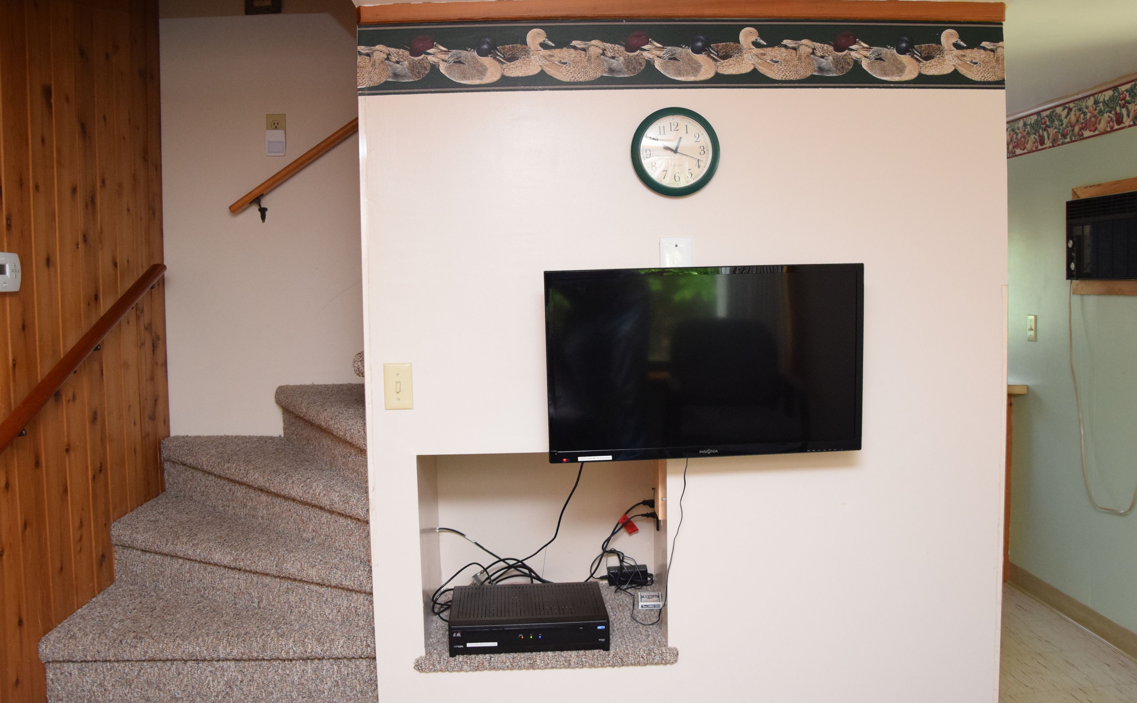Una escalera con barandilla de madera, un reloj de pared y un televisor de pantalla plana.