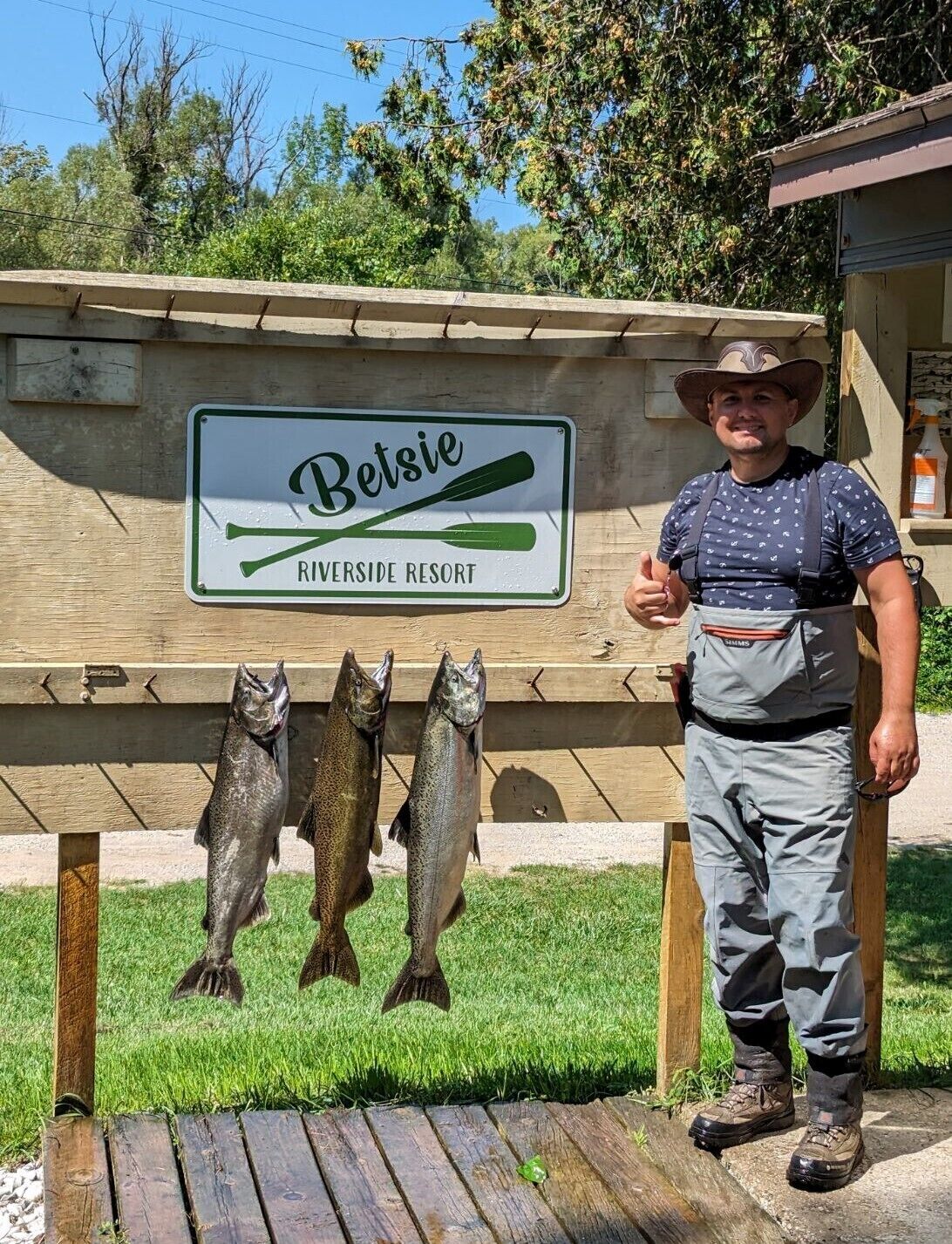 Une enseigne pour le Betsie Riverside Resort, avec une clôture en bois et deux poissons en décoration.