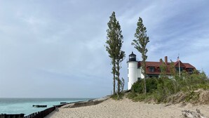 A sandy beach with a lighthouse and a house in the background. - Betsie Riverside Resort (Benzonia)