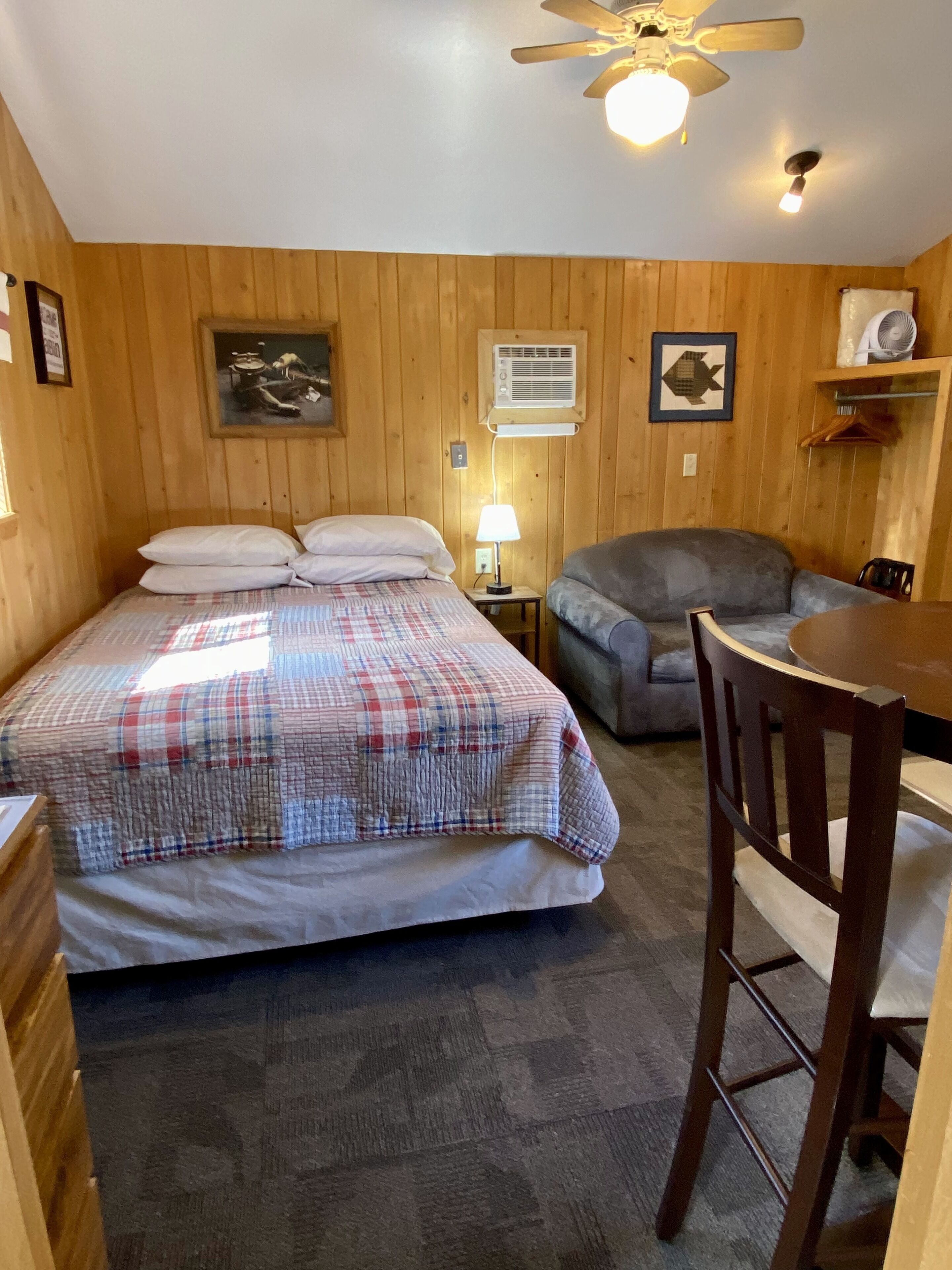 Une pièce en bois avec un lit, une chaise, une table et un ventilateur de plafond.