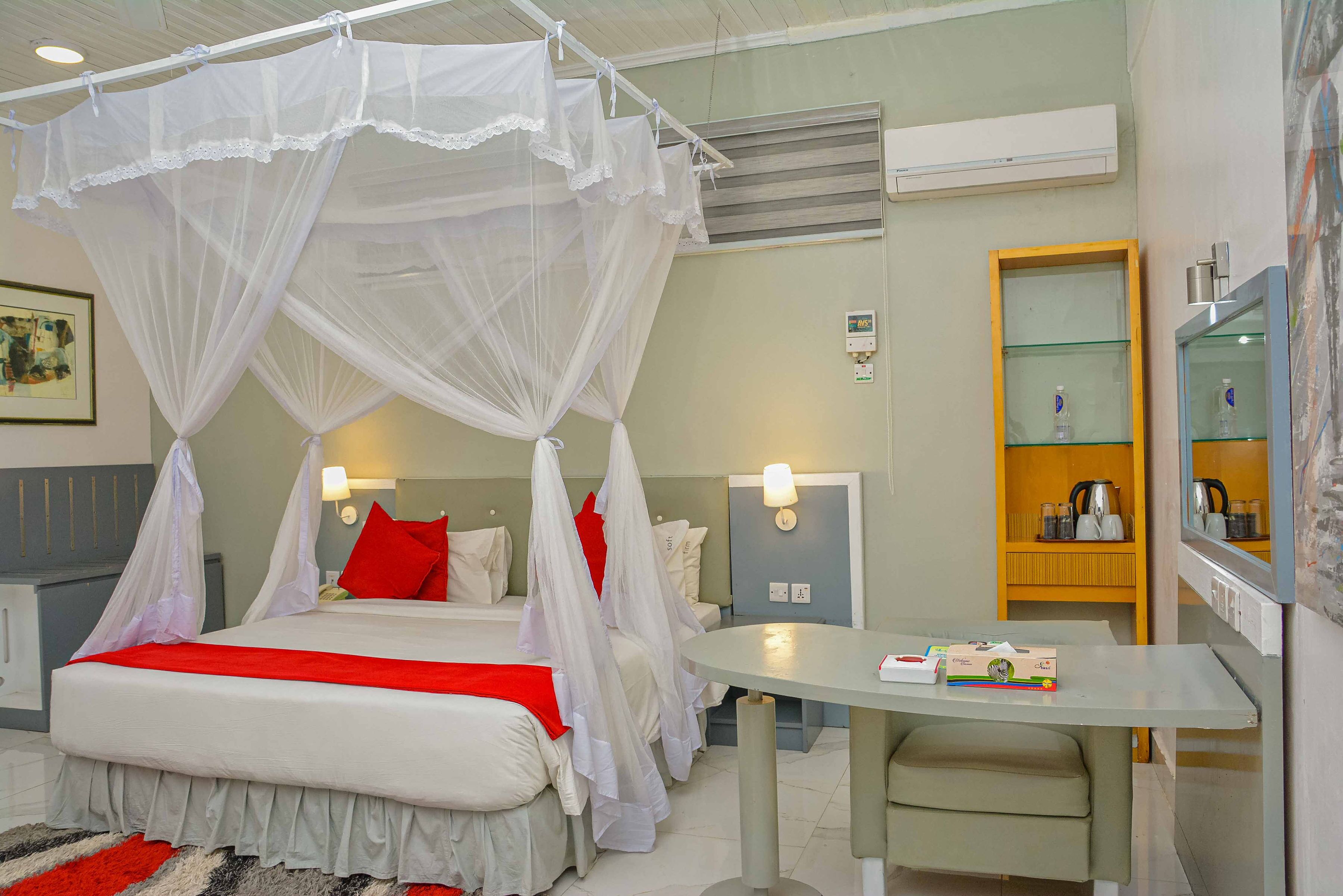 Habitación de hotel con cama con dosel, una mesa redonda, un espejo y una kitchenette.