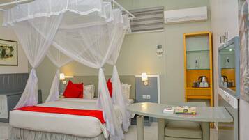 Habitación de hotel con cama con dosel, una mesa redonda, un espejo y una kitchenette.
