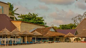 Un edificio frente a la playa con techos de paja y asientos al aire libre.