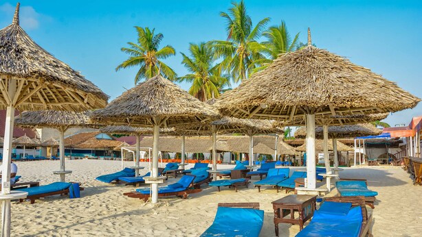 Una playa con sombrillas de paja y sillones de madera.