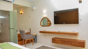 A modern hotel room with a bed, a desk, a chair, a TV, a mirror, and built-in wooden storage.