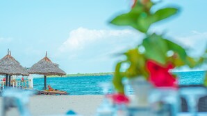 Escena de playa con dos sombrillas de paja y una terraza de madera.