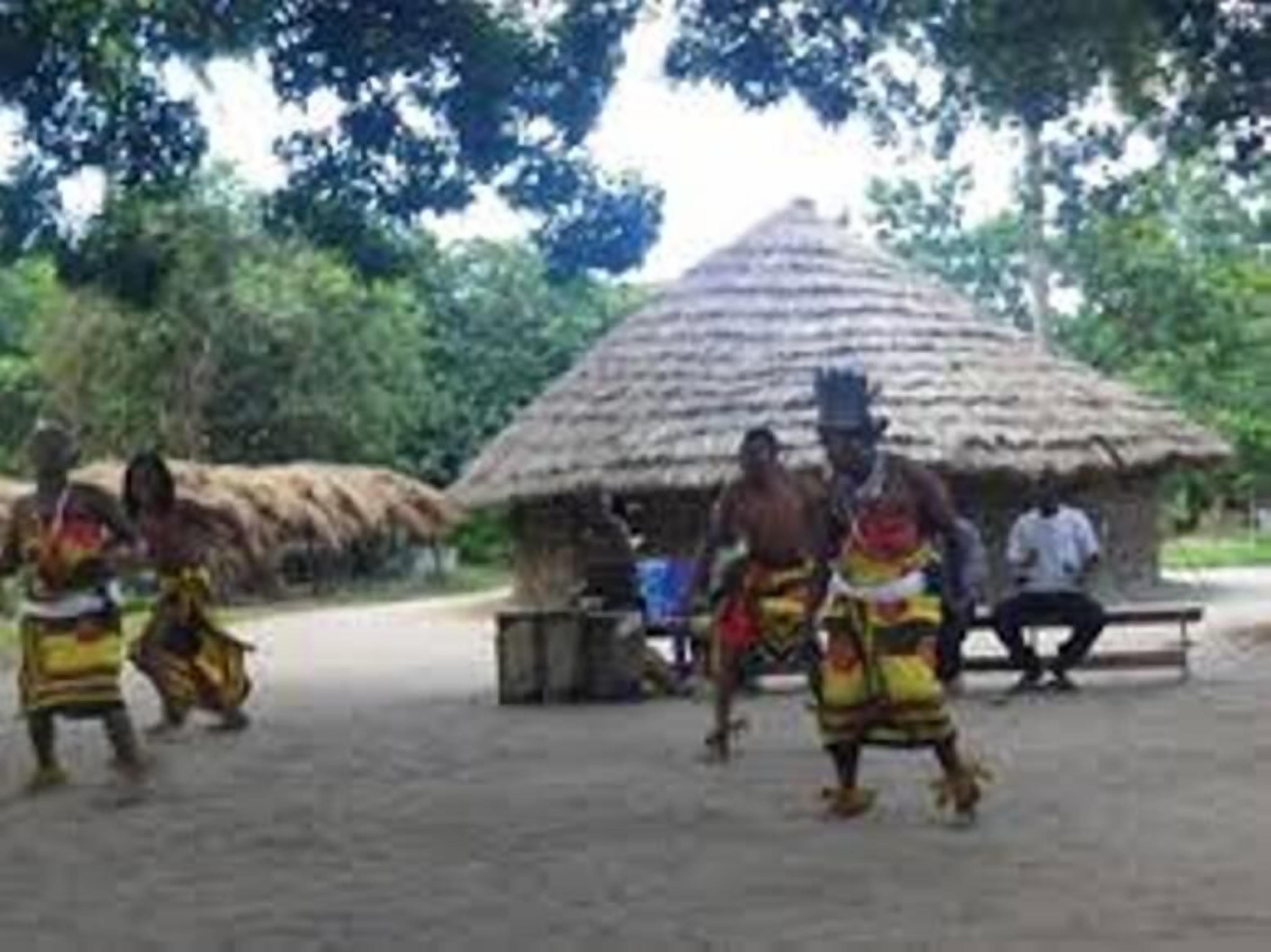 Un grupo de personas vestidas con atuendo tradicional bailando frente a una cabaña con techo de paja.