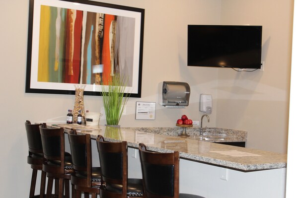 A modern kitchen with a granite countertop, a bar area with chairs, a flat-screen TV mounted on the wall, and a framed abstract painting above the counter. - Reston Lodge & Suites (Emmetsburg)