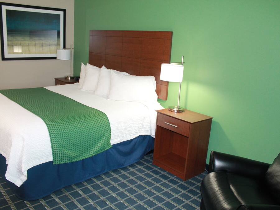 A hotel room with a large bed, a nightstand with a lamp, a wooden headboard, and a green wall.