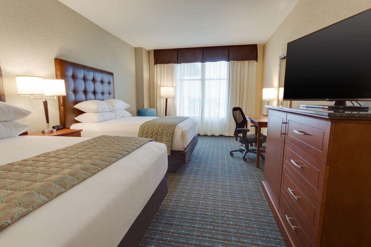 A hotel room with two beds, a desk, a television, and a chair.