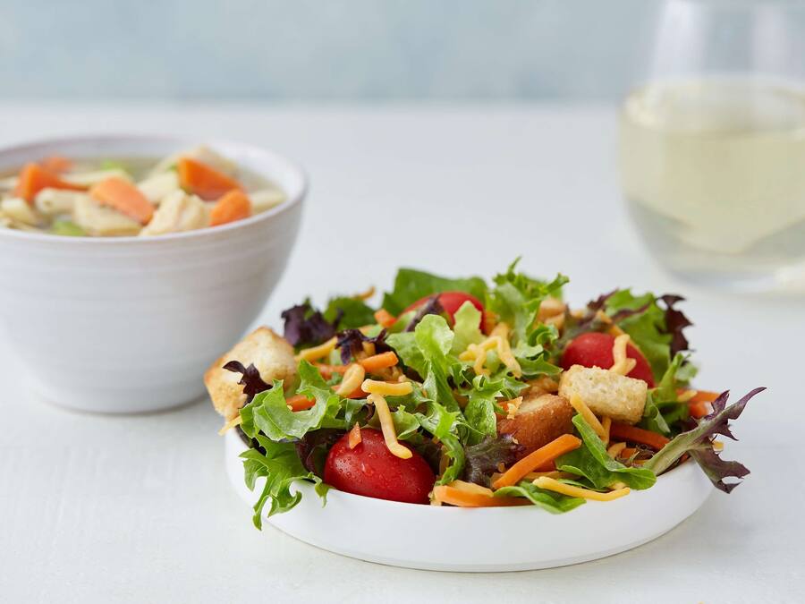 A bowl of soup and a salad with croutons and cheese on a white plate.