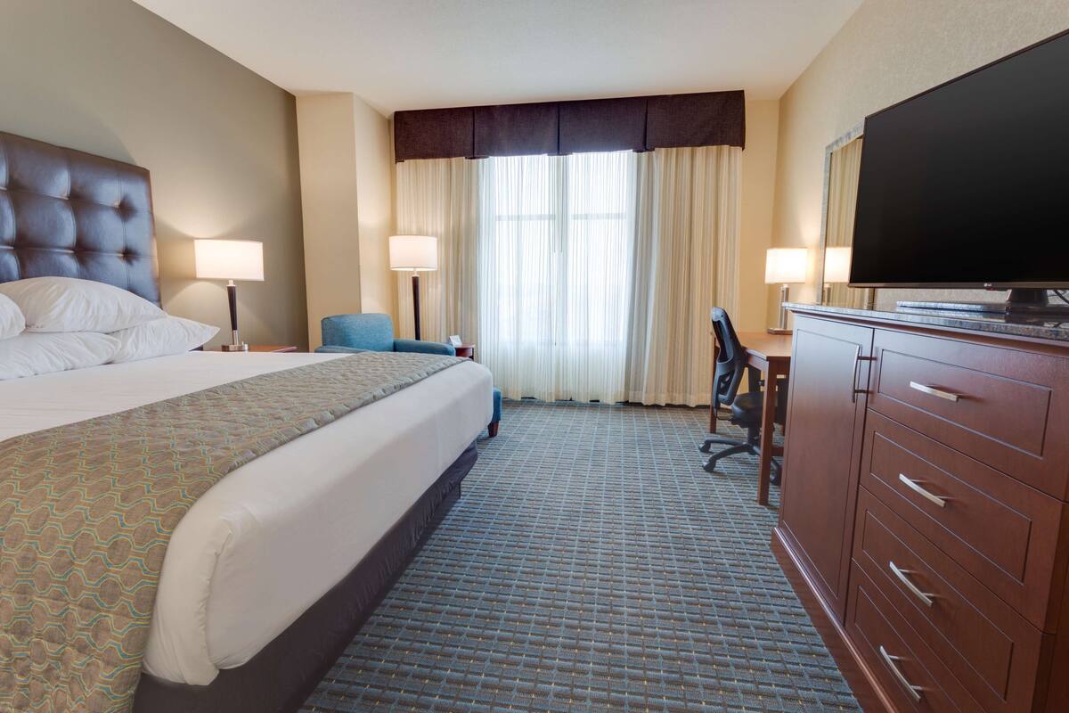 A hotel room with a large bed, a desk, a television, and a wardrobe.