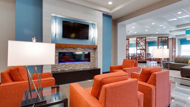 A modern lobby with orange seating, a flat-screen TV, and a stone accent wall. - Drury Plaza Hotel St. Louis St. Charles (St. Charles)