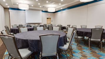 Un salón de conferencias con mesas redondas, sillas y una pantalla de proyector.