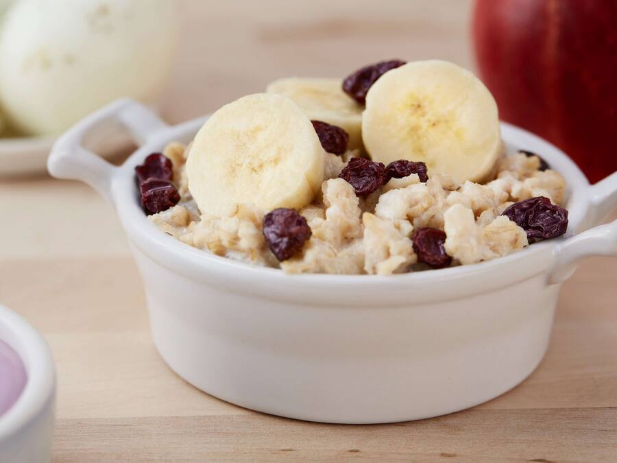 A bowl of oatmeal with bananas and raisins.