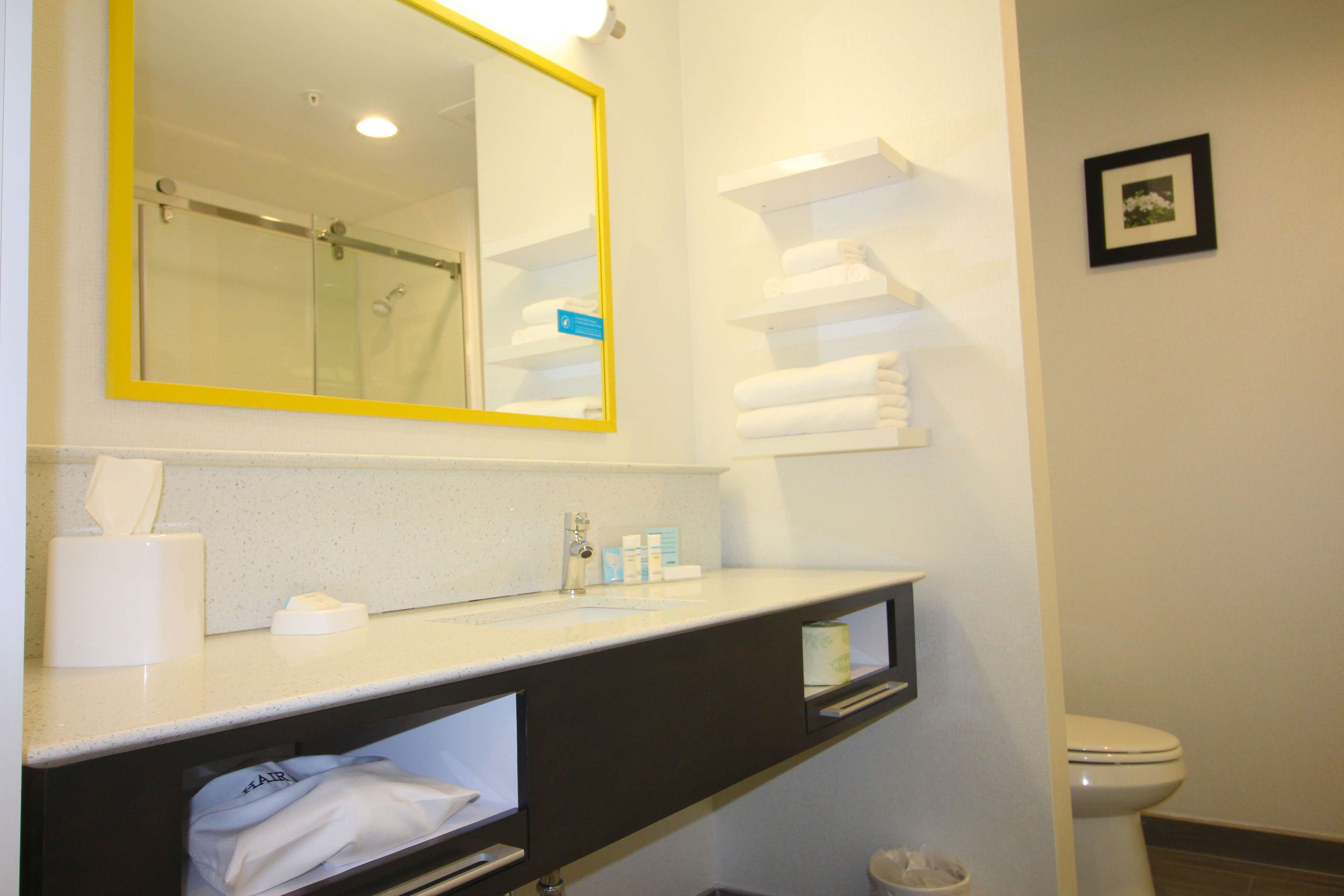 A bathroom with a mirror, towel rack, toilet, and a trash bin.