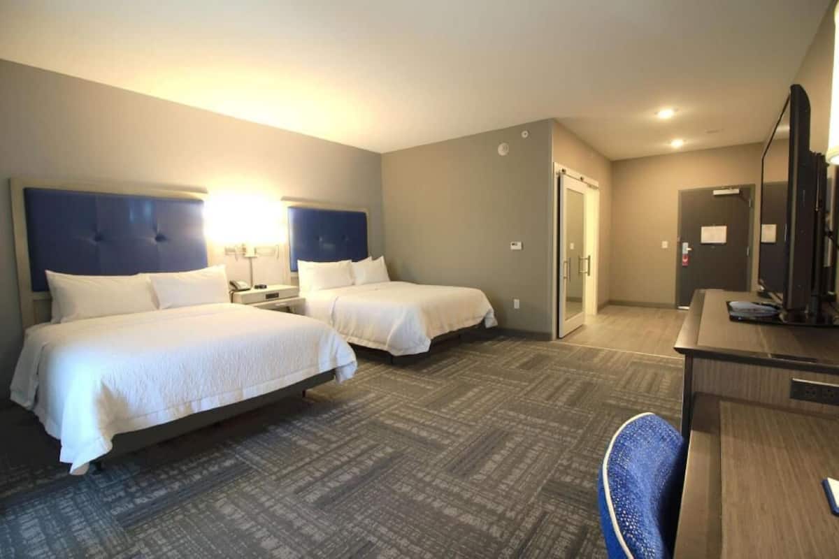 Une chambre d’hôtel avec deux lits, un bureau, une chaise et un téléviseur.