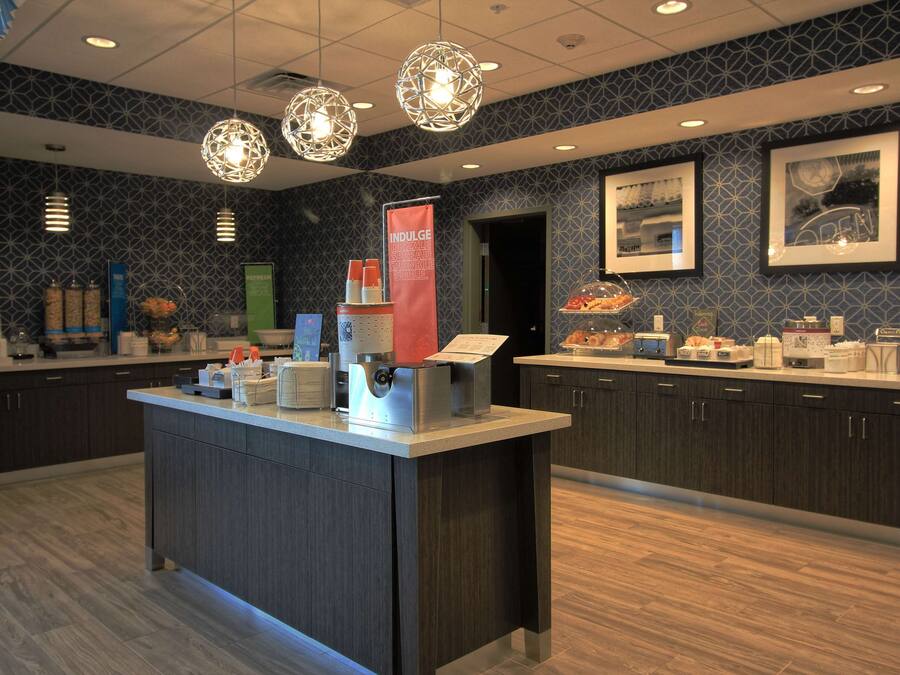 A modern hotel lobby with a central reception desk, a coffee station, and a buffet area.