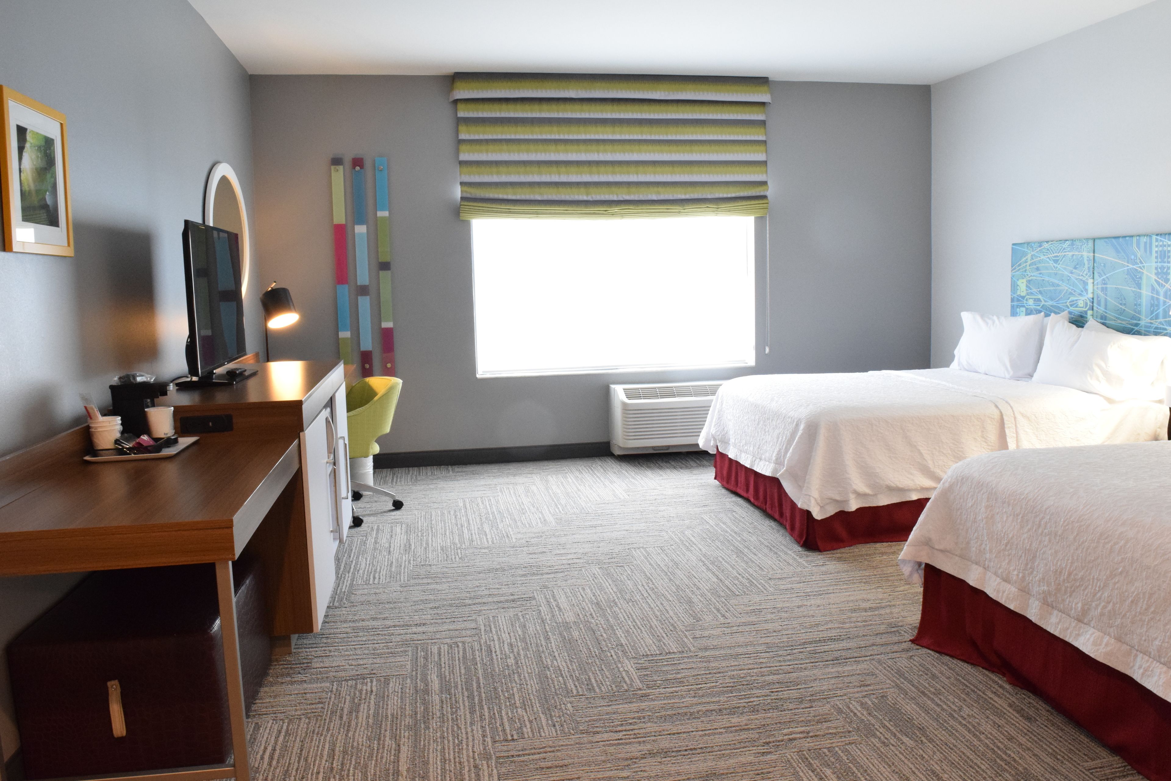 Habitación de hotel con un escritorio de madera, una silla, una cama con ropa de cama blanca, una ventana con persiana a rayas y un cuadro con un mapa en la pared.