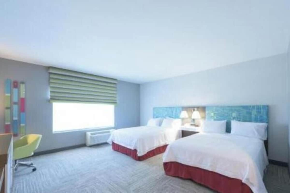 A hotel room with two beds, a desk, a chair, and a window with blinds.