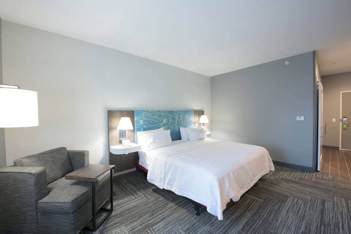 A hotel room with a bed, a desk, a chair, a nightstand, and a wall with a map.
