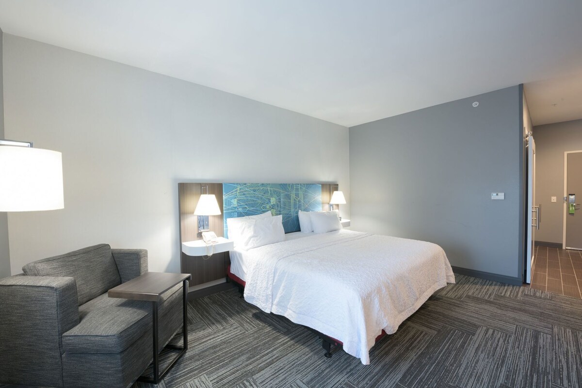 A hotel room with a bed, a desk, a chair, a nightstand, and a wall with a map.