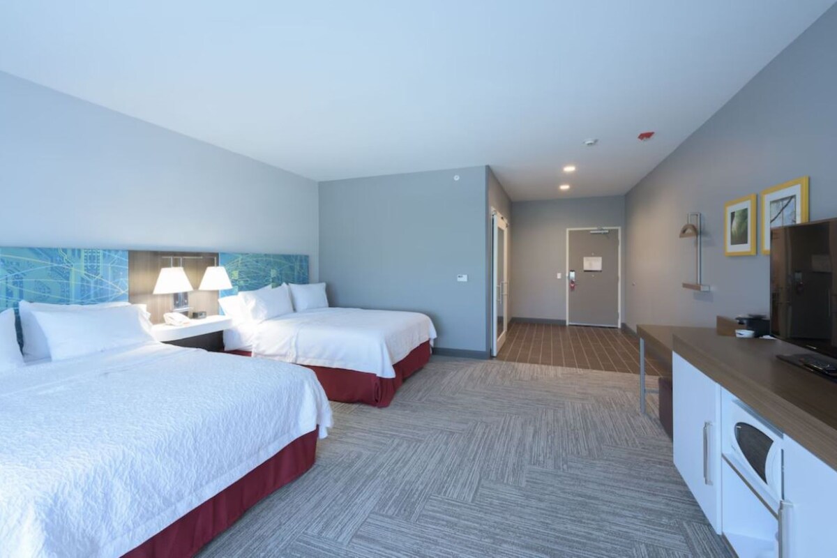 A hotel room with two beds, a desk, a television, and a door leading to a hallway.