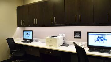 An office with two desks, each with a computer and a printer. There are two chairs, a cabinet above the desks, and a sign on the wall.