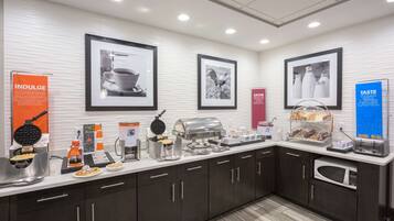 A modern kitchen with a buffet setup, including a waffle maker, coffee station, and various food items.
