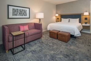 A hotel room with a bed, a sofa, a small table, two storage boxes, and two wall-mounted lamps. - Hampton Inn & Suites Portland-Pearl District (Portland)