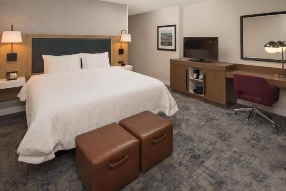 A hotel room with a large bed, a desk with a chair, a television, and a mirror.