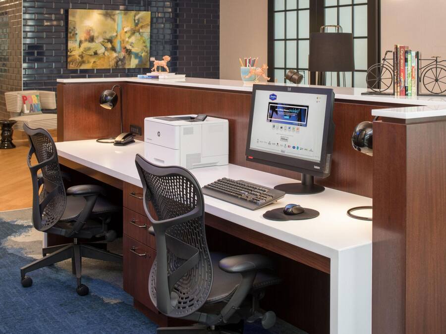 A modern office cubicle with a desktop computer, printer, and two office chairs.
