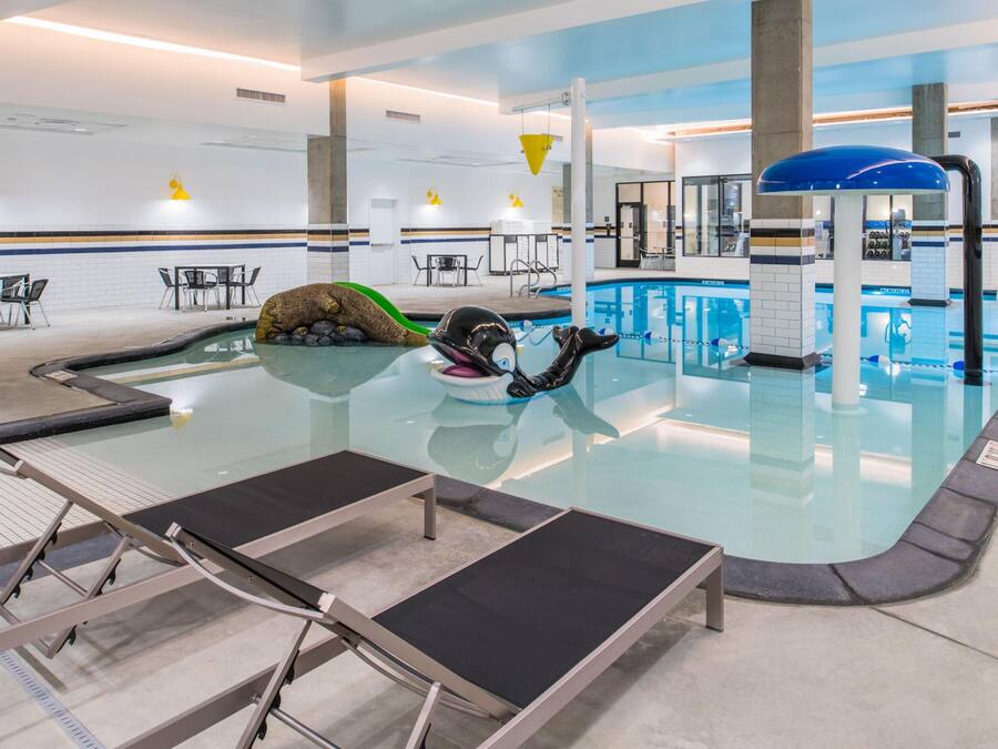 An indoor swimming pool with lounge chairs, a diving board, and a lifeguard stand.