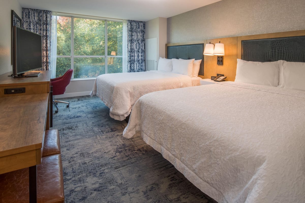 A hotel room with two beds, a desk with a TV, a chair, and a window with curtains.