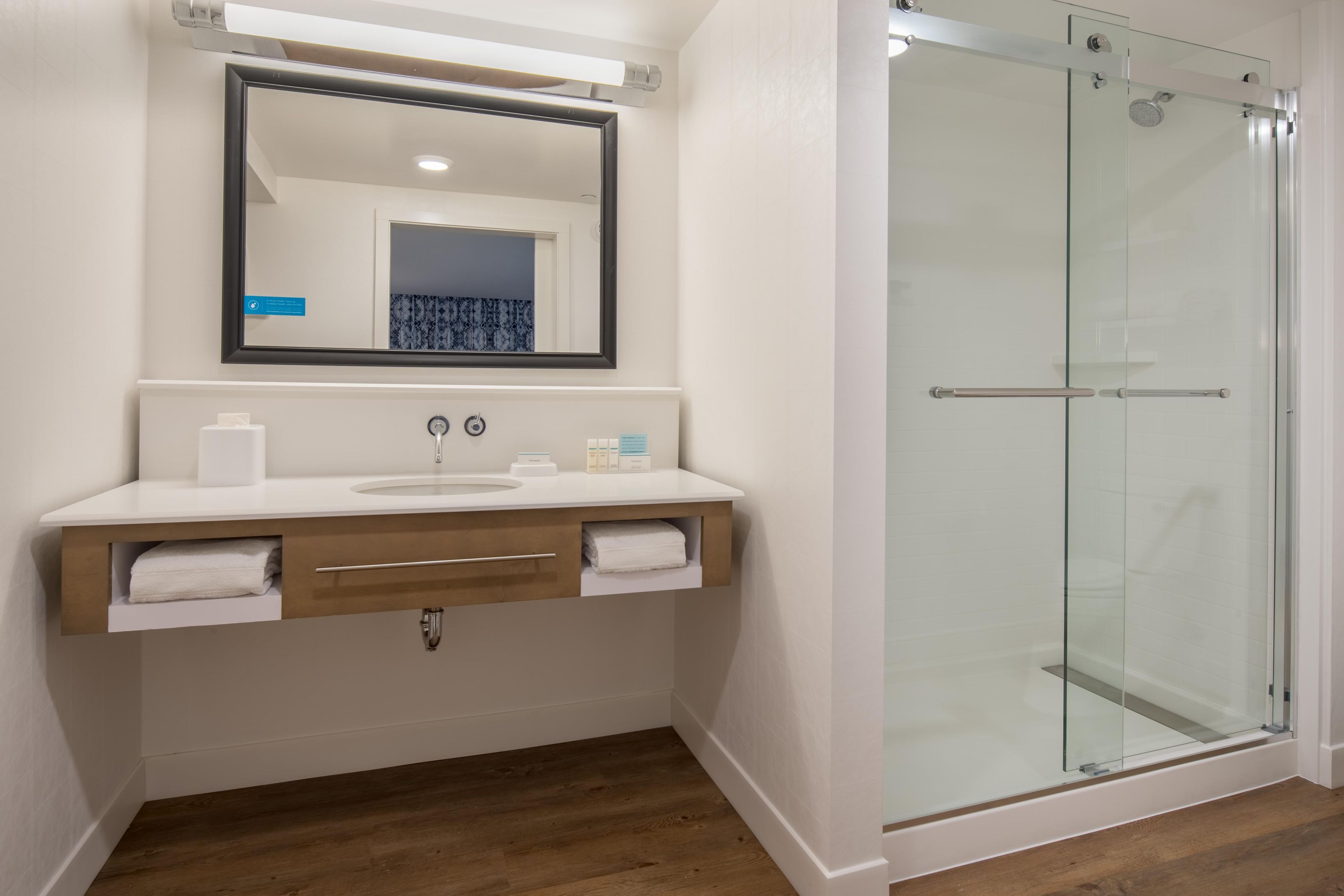 A modern bathroom with a glass shower enclosure, a white sink with a wooden vanity, and a large mirror above the vanity.
