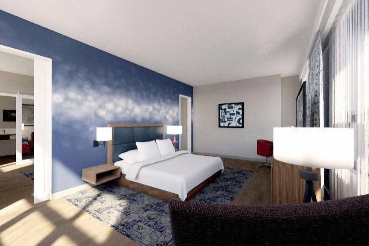 A modern hotel room with a large bed, a desk, a chair, and a TV.