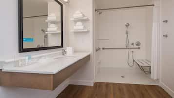 A modern bathroom with a large mirror, a sink with toiletries, and a walk-in shower.